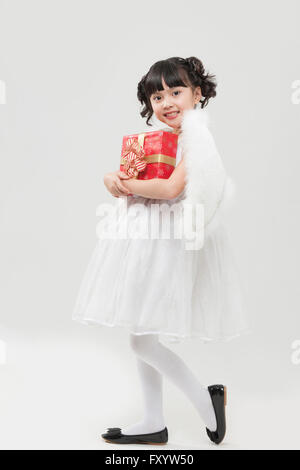 Seitenansicht des lächelndes Mädchen gekleidet wie ein Engel hält eine Geschenkbox starrte auf Vorderseite Stockfoto