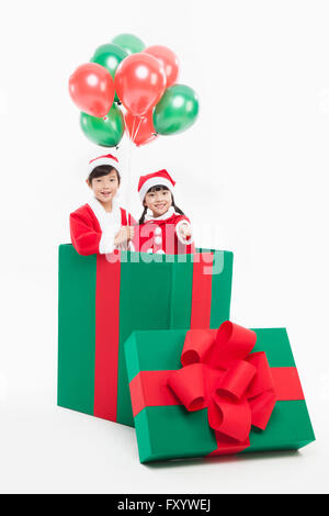 Porträt von lächelnden jungen und Mädchen in Santas Kleidung mit Ballons in eine große Geschenkbox starrte auf Vorderseite Stockfoto