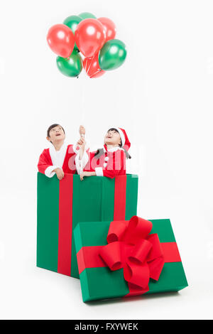 Porträt der jungen und Mädchen in Santas Kleidung mit Ballons in eine große Geschenkbox nachschlagen Stockfoto