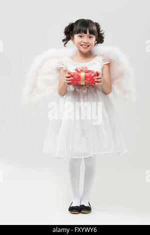 Lächelndes Mädchen gekleidet wie ein Engel stehend mit einer Geschenkbox Stockfoto