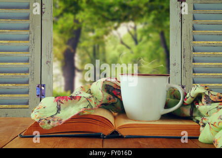 romantische Szene Tasse Kaffee neben alten Buch vor Blick auf die Landschaft außerhalb des alten rustikalen Fensters. Jahrgang gefiltert Stockfoto