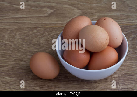 Eine weiße Schüssel voll mit frischem, braun gesprenkelten Eiern auf einem Holztisch. Stockfoto