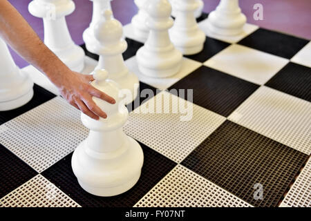 Hand bewegt den schwarzen Bauern auf einem Riesen-Schach-Spiel Stockfoto