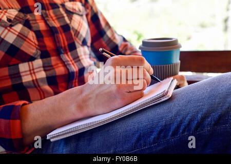Closeup von einem kaukasischen Jüngling trägt Jeans und ein kariertes Hemd mit einem Stift in ein Notizbuch schreiben Stockfoto
