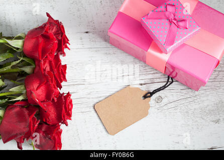 Romantische Geschenk-Konzept mit roten Rosen, Geschenkboxen und leere Tag auf weißem rustikalen Holztisch. Draufsicht mit Textfreiraum. Stockfoto