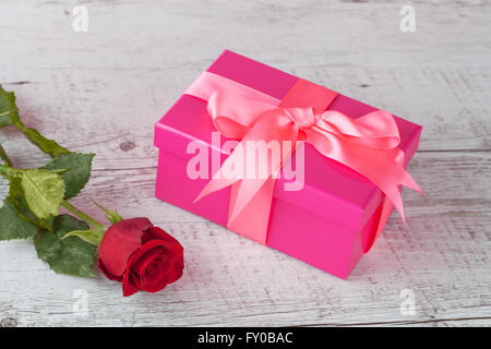 Eine rote rose und pink Geschenk-Box mit Band auf weißem rustikalen Holztisch mit Textfreiraum. Stockfoto