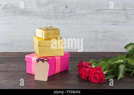 Drei rote Rosen und drei Geschenk-Boxen mit leeren Tag auf Holztisch mit Textfreiraum Stockfoto