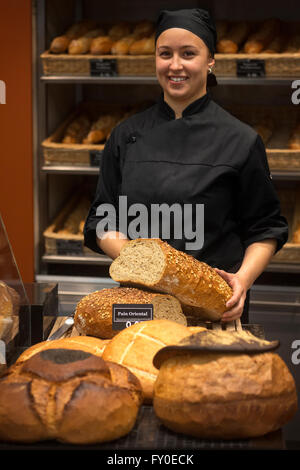 Ein Lächeln auf den Lippen Bäckersfrau präsentiert sie Brote Brot. Bäckerei-Verkäuferin in schwarzer Uniform hält Laib Brot. Stockfoto