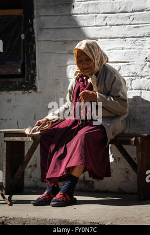 Ältere Frau purpurnen Gewand trägt und hält buddhistischen Gebetsperlen sitzen auf Holzbank in Trongsa, Bhutan Stockfoto