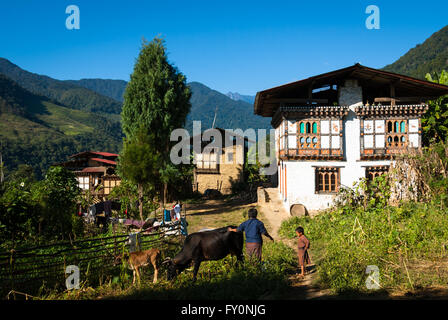 Frau und Kind mit Vieh vor traditionellen Bauernhof befindet sich in Nabji Dorf im südlichen Bhutan Stockfoto