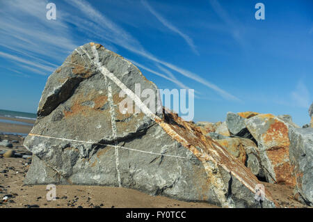 Ein großes Stück Fels mit Quart Adern durchschneiden sie am Strand, vor blauem Himmel mit Jet Kondensstreifen. Stockfoto