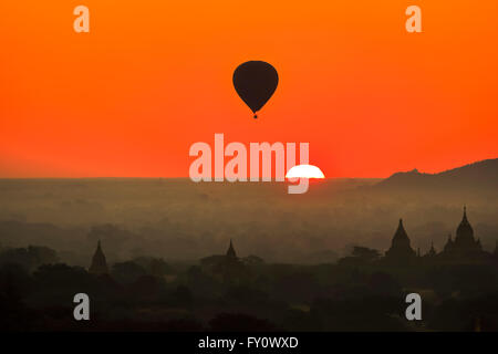 Sonne über den Horizont und Heißluft Ballon fliegen bei Old Bagan mit orangefarbenen Himmel und Tempel Silhouetten, Myanmar (Burma) Stockfoto