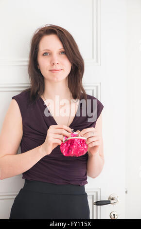 Porträt der Frau hält eine rote Geldbörse. Lebensstil-Bild der jungen Frau im schwarzen Kleid zeigt stolz, Zuversicht und Zufriedenheit. Stockfoto