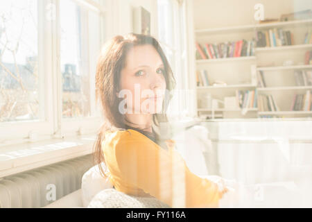 Frau sitzt im Wohnzimmer, Blick aus dem Fenster. Sie haben einen Gesichtsausdruck von Traurigkeit, Einsamkeit und Wut. Stockfoto