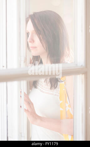 Frau am Fenster stehend, wegschauen. Konzept der Traurigkeit, warten und Vorfreude. Lifestyle-Bild der Kontemplation. Stockfoto