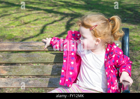 Kleinkind Mädchen suchen seitwärts sitzen auf Bank Stockfoto