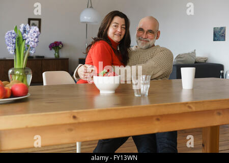 Porträt von glücklich älteres paar umarmt und Holztisch zu Hause sitzen Stockfoto