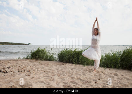 Junge Frau praktizieren Yoga am Ufer des Meeres gegen Himmel Stockfoto