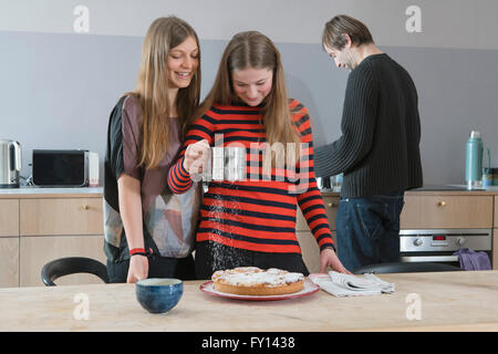 Junge Frau beobachtete Schwester Beregnung-Tarte mit Puderzucker in Küche Stockfoto