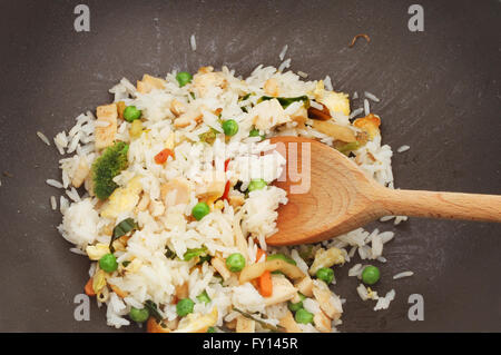 Nahaufnahme von Huhn, Ei und Gemüse rühren gebratenen Reis im Wok mit einem Holzlöffel Stockfoto