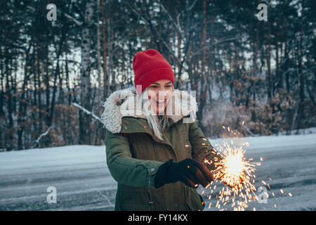 Glückliche Frau mit Wunderkerzen stehend auf Feld im winter Stockfoto