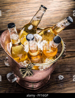 Kalte Flaschen Bier in den ehernen Eimer auf dem Holztisch. Stockfoto