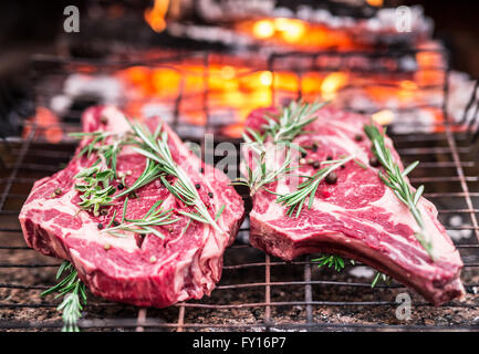 Rib-Eye-Steaks und Grill mit brennendem Feuer hinter ihnen. Stockfoto