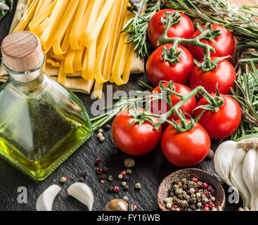 Pasta Zutaten. Cherry-Tomaten, Spaghetti Nudeln, Rosmarin und Gewürze auf einem Graphit-Brett. Stockfoto