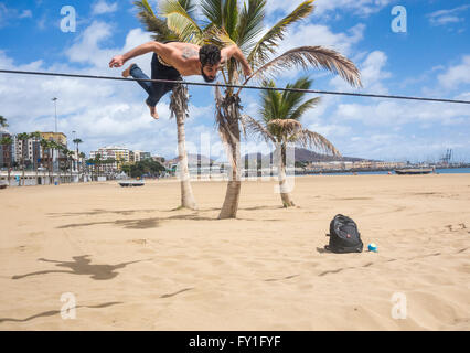 Mann, Saltos und Gymnastik demontiert auf slackline zwischen Palmen am Strand in Spanien gebunden Stockfoto