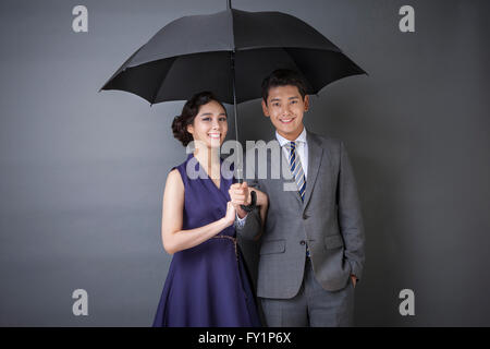 Junge Paar in Retro-Styles teilen einen Regenschirm starrte auf Vorderseite lächelnd Stockfoto