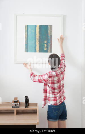 Wieder hängen der jungen Frau einen Bilderrahmen an der Wand nach oben Stockfoto