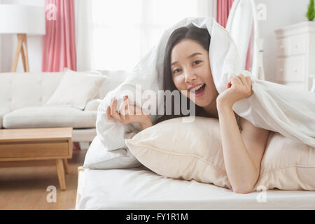 Porträt des jungen lächelnde Frau liegend auf Bett deckt sich mit einer Decke starrte auf Vorderseite Stockfoto