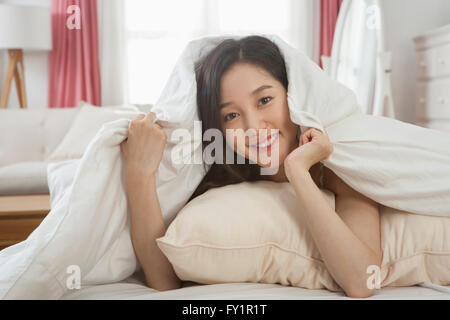 Porträt des jungen lächelnde Frau liegend auf dem Bett, die sich mit einer Decke zu bedecken Stockfoto