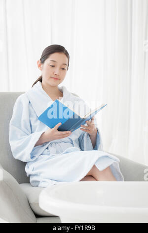 Junge Frau im Kleid auf Sofa sitzen und ein Buch mit einer Badewanne Stockfoto
