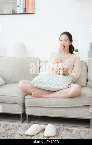 Junge Frau sitzt auf dem Sofa Essen popcorn Stockfoto