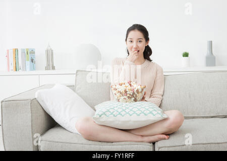 Junge lächelnde Frau sitzend auf Sofa Essen popcorn Stockfoto