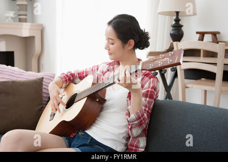 Seitenansicht der Frau sitzt auf dem Sofa eine Gitarre spielen Stockfoto