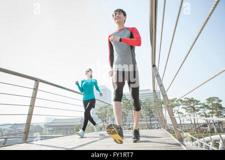 Niedrigen Winkel Blick auf junge lächelnde paar Joggen im park Stockfoto