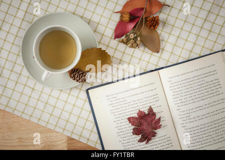 Hintergrund des Herbstes mit einer Tasse Tee, offenes Buch und Laub auf Tischdecke Stockfoto