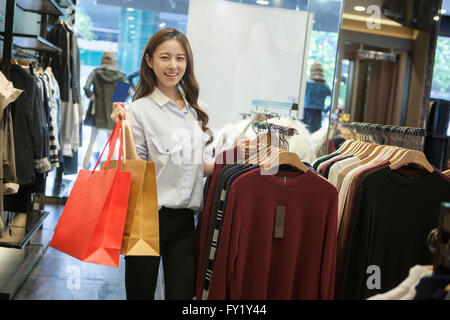 Frau hält Einkaufstaschen und lächelnd durch Kleiderbügel in einem shop Stockfoto