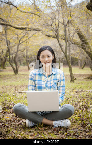 Frau am Boden sitzen und arbeiten an ihrem Laptop mit einem Lächeln im Herbst Stockfoto