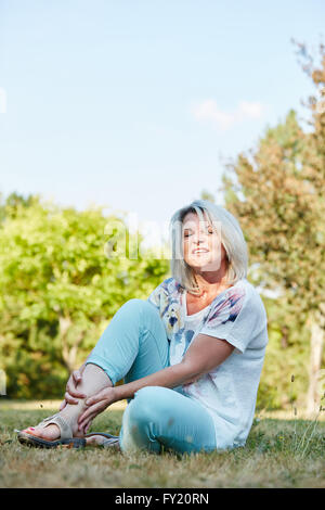 Alte Frau mit Schmerzen hält ihren Fuß in der Natur Stockfoto