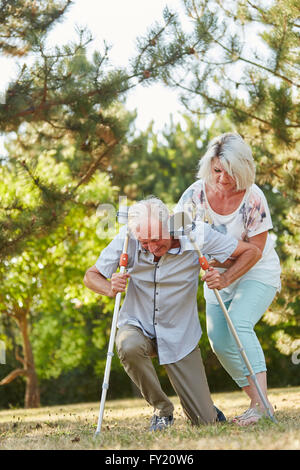 Frau hilft Mann auf Krücken aufzustehen in der Reha Stockfoto