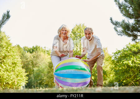 Älteres Paar spielen und glücklich lächelnd mit einem Ball im Sommer Stockfoto