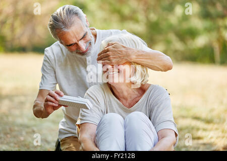 Alter Mann überrascht Frau mit einem Geschenk zum Geburtstag in einem Garten im Sommer Stockfoto