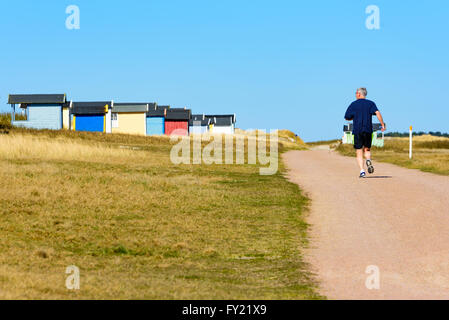 Skanor, Schweden - 11. April 2016: Erwachsener Mann wegläuft, Sie auf einem Wanderweg an einem Strand mit vielen Hütten neben Baden Stockfoto