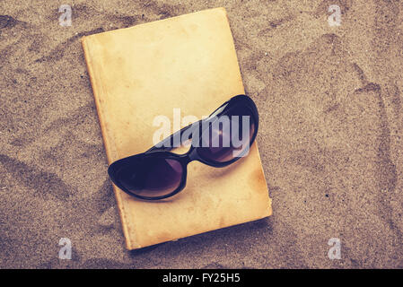 Lesen Sie alte Lieblingsbuch im Sommer Urlaub Strandurlaub, Draufsicht eines Buches und Sonnenbrillen in warmen Strand Schnee. Stockfoto