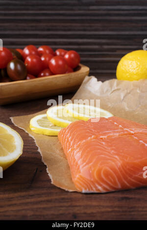 Roher Lachs auf Papier, Cherry-Tomaten, Zitrone und Petersilie backen. Rustikale Holz Hintergrund Stockfoto