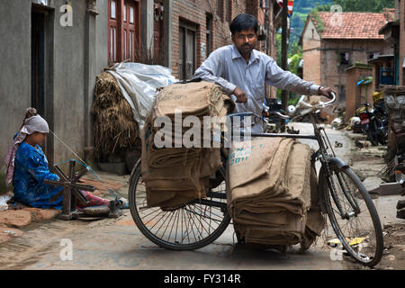 Ein Mann mit einem alten Fahrrad und eine Frau spinnt Wolle in dem kleinen Dorf Bungamati, Nepal Stockfoto