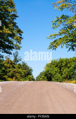 Leeren braunen Land dirt road Hill gegen leere blaue Himmel und die umliegenden Bäume auf beiden Seiten und im Hintergrund. Stockfoto